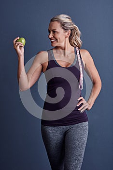 The power is in your hands. Studio shot of an attractive mature woman holding an apple against a blue background.