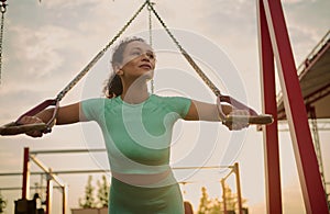 Powerful attractive muscular African American woman fitness trainer do battle workout with ropes, suspension straps in the outdoor