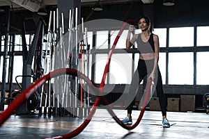 Powerful attractive muscular woman CrossFit trainer do battle workout with ropes at the gym