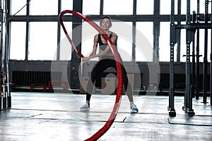 Powerful attractive muscular woman CrossFit trainer do battle workout with ropes at the gym