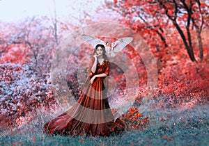 Powerful autumn nymph, queen of fire and goddess of hot sun, lady in long red light dress with loose sleeves with dark