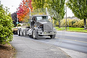 Powerful big rig black semi truck with step down semi trailer and sign for transporting oversize load running on the local road