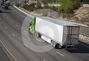 Powerful big rig green bonnet semi truck transporting frozen cargo in refrigerated semi trailer driving on the wide multiline