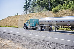 Powerful big rig semi truck tractor transporting fuel in long tank semi trailer climbing on up hill road