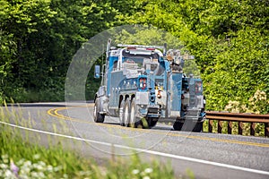 Powerful big rig towing truck for tow semi trucks running on the winding road in green forest