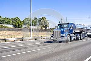 Powerful blue day cab big rig semi truck transporting liquid cargo in shiny tank semi trailer driving on the straight multiline