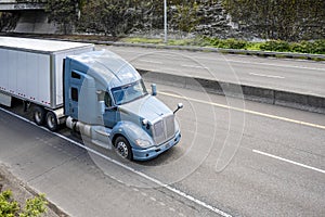 Powerful blue gray big rig semi truck transporting cargo in dry van semi trailer driving on the divided lower highway road