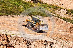 A powerful bulldozer in a sand pit is planning a site. Extraction of sand in an open pit. natural building materials