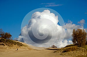 Powerful clouds and man walking up a sand dune