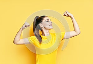 Powerful confident young woman showing arms muscles on yellow background