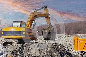 A powerful crawler excavator loads the earth into a dump truck against the blue sky. Development and removal of soil from the