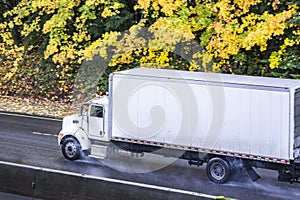 Powerful day cab big rig white semi truck transporting goods in long box trailer driving on the autumn road at rain time