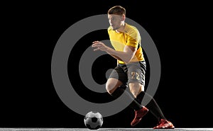 Powerful, flying above the field. Young football, soccer player in action, motion isolated on black studio background .