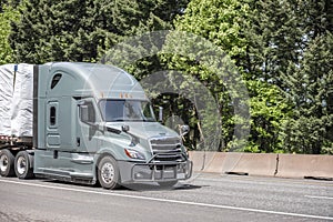 Powerful gray big rig semi truck with pipes grille guard transporting covered by tarp commercial cargo on the flat bed semi