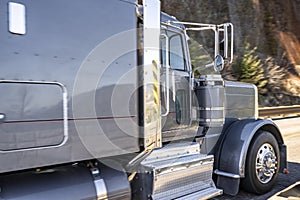 Powerful gray classic big rig semi truck tractor with chrome parts transporting cargo running on the narrow mountain road along