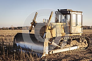 Powerful heavy crawler bulldozer works at a construction site in the evening against the background of the sunset sky.