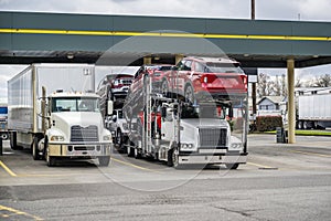 Powerful industrial big rig semi trucks with dry van and car hauler loaded semi trailers standing on the truck stop parking lot