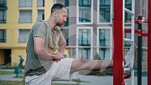 Powerful latino man american athletic sportsman guy stand in side bend position inclining to wall bars on sports ground