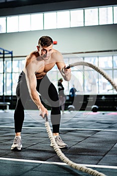 powerful man training battle ropes at cardio workout in dark gym. Professional athlete exercise fitness sport club equipment.