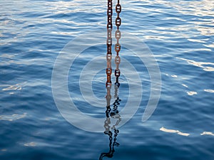 Powerful metal chain going into the water. Deep sea work. An industrial tool lowered into the depths of the sea