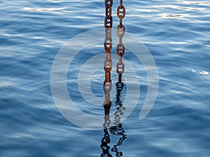 Powerful metal chain going into the water. Deep sea work. An industrial tool lowered into the depths of the sea