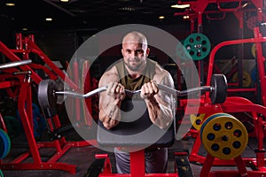 Powerful muscular man doing biceps exercise with barbell on the bench