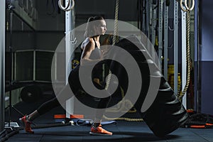 Powerful muscular woman CrossFit trainer doing tire workout at gym