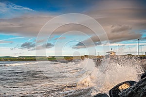 Powerful ocean wave crushes on stone shore. West coast of Ireland, Lahinch town, county Clare. Warm sunny with cloudy sky,
