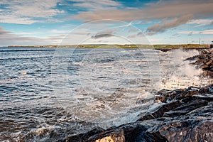 Powerful ocean wave crushes on stone shore. West coast of Ireland, Lahinch town, county Clare. Warm sunny with cloudy sky,