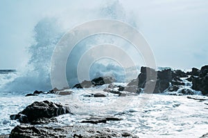 Powerful ocean wave splashes across a big rock.