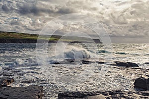 Powerful ocean waves hit rough stone coast. Doolin, county Clare, Ireland. Dark dramatic light and cloudy sky. Irish landscape.