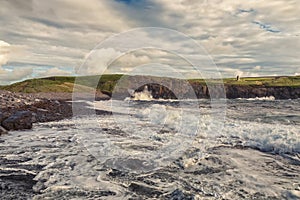 Powerful ocean waves hit rough stone coast. Doolin, county Clare, Ireland. Dark dramatic light and cloudy sky. Irish landscape.