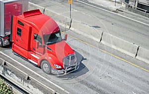 Powerful red big rig long haul semi truck transporting cargo in semi trailer running on the divided highway