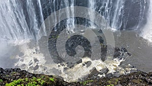 Powerful streams of Victoria Falls fall into the gorge. At the bottom are black stones.