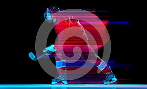Powerful throw. Male ice hockey player in sports protective uniform in action over dark background in neon mixed light