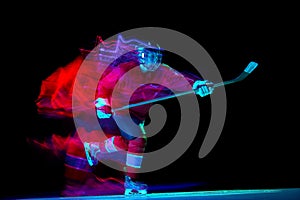 Powerful throw. Male ice hockey player in sports protective uniform in action over dark background in neon mixed light