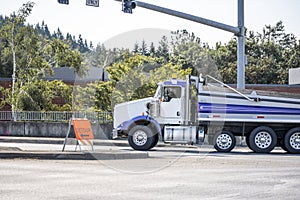 Powerful tip truck with covered trailer running on the city street crossroad with traffic light and detour road sign