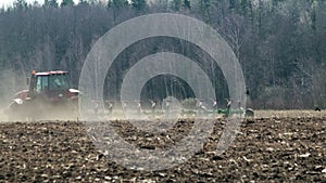 Powerful tractor with a plow drives through dusty and arid farmland in hot weather. Soil erosion