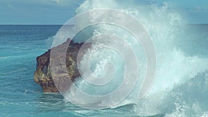 Powerful turquoise ocean wave splashes across a big rock in the middle of sea