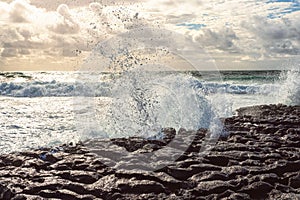 Powerful wave crushes against ragged stone coast creating splash of water. Dark dramatic light. Atlantic ocean, Doolin area,
