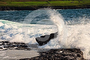 Powerful wave crushes against ragged stone coast creating splash of water. Dark dramatic light. Atlantic ocean, Doolin area,