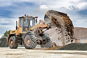 Powerful wheel loader or bulldozer against the sky. Loader pours sand from bucket. Powerful modern equipment for earthworks and