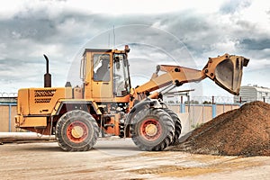 Powerful wheel loader or bulldozer at the construction site. Loader transports sand in a storage bucket. Powerful modern equipment