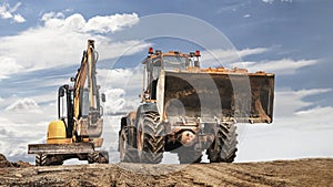 Powerful wheel loader or bulldozer working and mini excavator against blue cloudy sky. Modern equipment for earthworks. Rental of