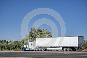 Powerful white classic big rig bonnet semi truck transporting cargo in reefer semi trailer moving on the road for timely delivery