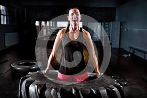 Powerful woman lifting big tire at intense training