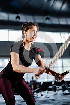 Powerful woman training battle ropes at cardio workout in dark gym. Professional athlete exercise fitness sport club equipment.
