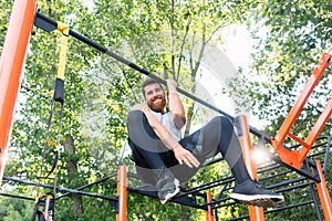 Powerful young man doing one-arm pull-ups while hanging on a bar