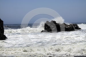 Powerfull waves crashing on a rock and splashing water in the air on remote black lava sand beach at Pacific coast