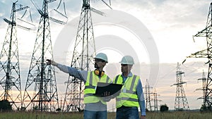 Powermen are discussing a project next to electrical towers